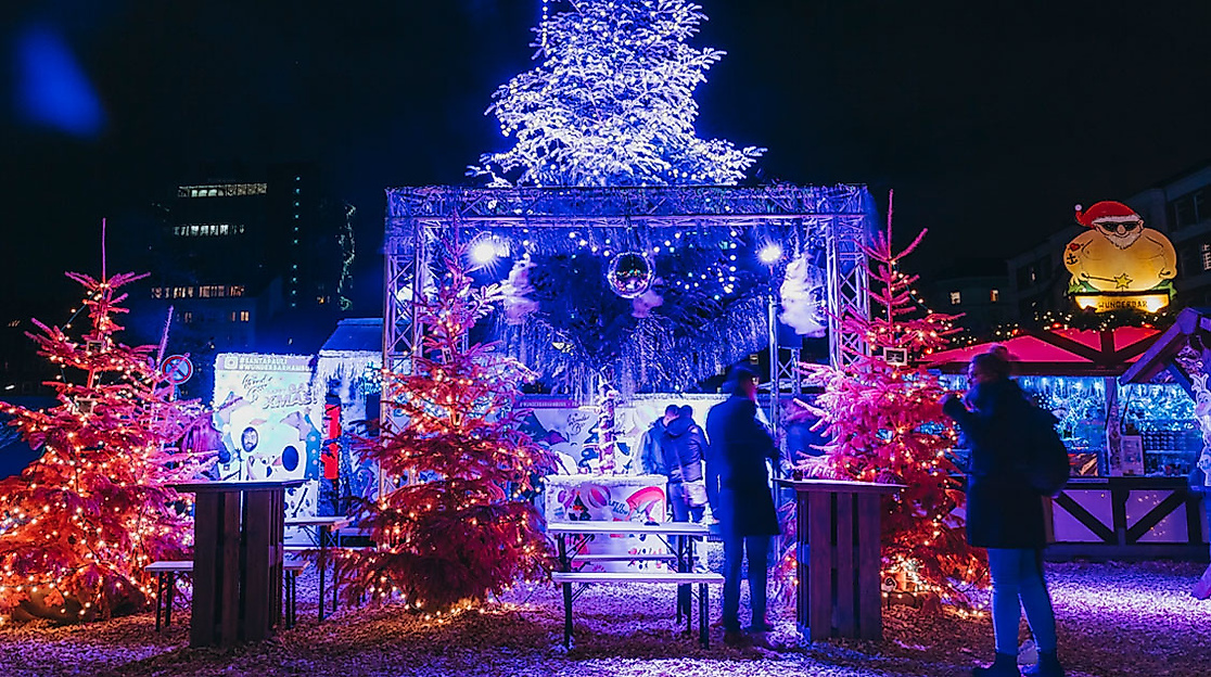 Bunt beleuchteter Weihnachtsmarkt Santa Pauli in Hamburg mit leuchtenden Bäumen und Besucher:innen am Abend