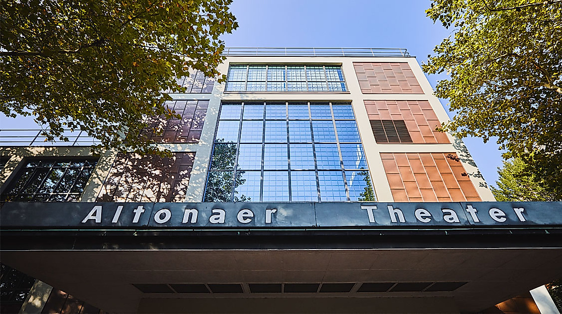 Außenansicht des Altonaer Theaters in Hamburg mit moderner Fassade und grüner Baumumrahmung bei Sonnenschein.
