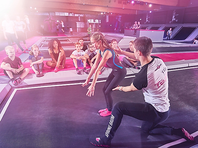 Gruppe junger Menschen beim Trampolinspringen im Sprungraum Hamburg mit Trainer und bunter Beleuchtung