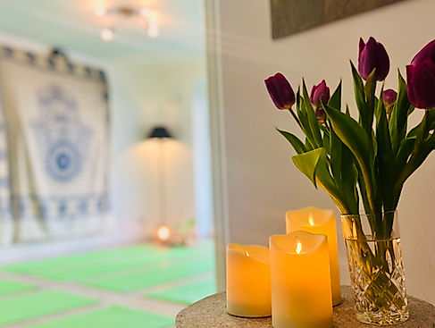 Achtsamkeitsraum mit Kerzen und Blumen. Im Hintergrund liegen Yogamatten für das Yoga- und Achtsamkeitswochenende.