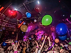 Bunte Party mit Luftballons, Lichteffekten und jubelndem Publikum in ausgelassener Queer-Bar-Atmosphäre