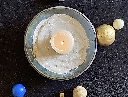 Eine brennende Kerze in einer mit Sand gefüllten Schale und ein Kreuz und Perlen darum herum