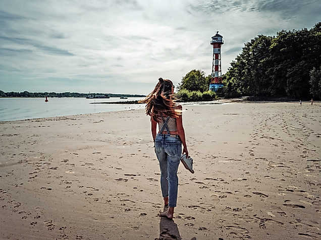 Frau trägt Kind am Elbstrand Wittenbergen, barfuß im Sand mit Leuchtturm im Hintergrund