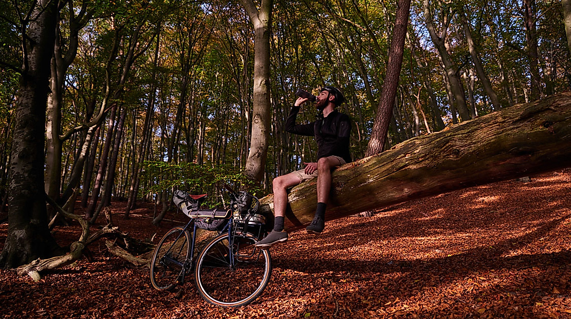Radfahrer pausiert auf Baumstamm im herbstlichen Wald und genießt die Natur bei Sonnenlicht