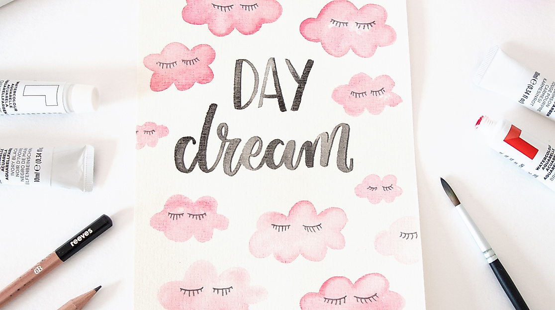 reatives Lettering mit „Daydream“ auf Papier, verziert mit rosa Wolken, Pinseln und Farben auf hellem Tisch