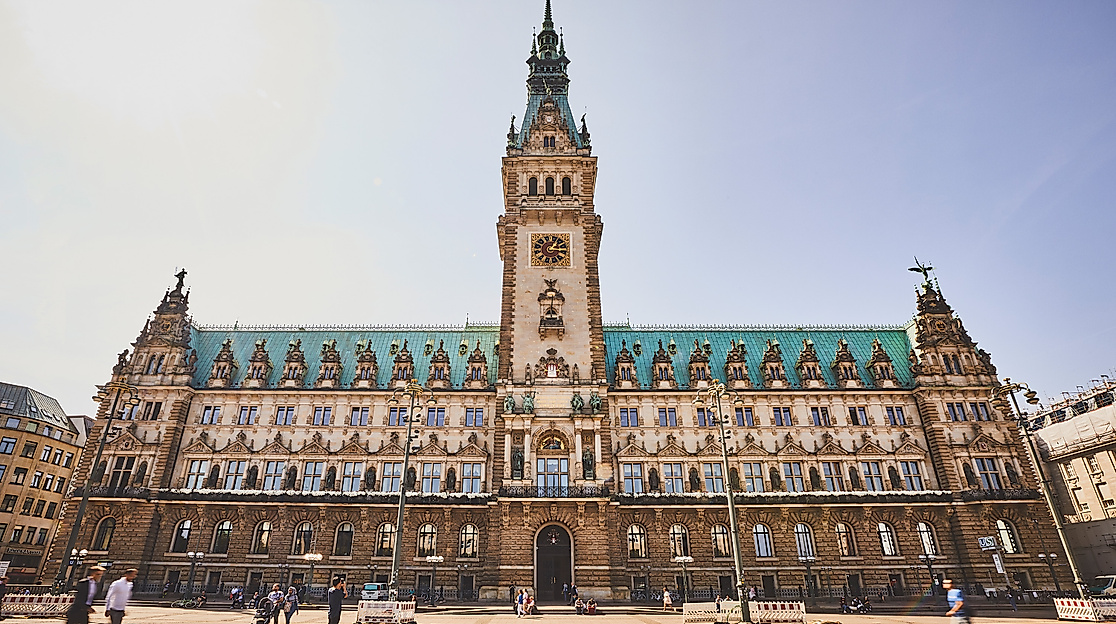 Hamburger Rathaus in Frontalansicht bei Sonnenschein vom Rathausmarkt aus mit Passant:innen