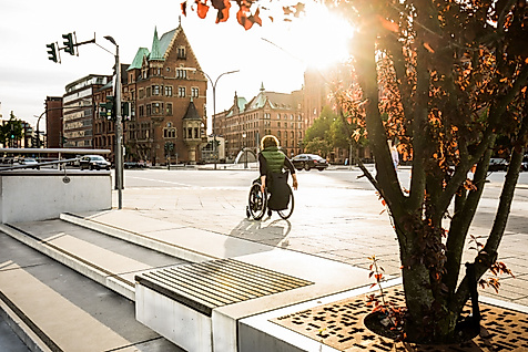 Person im Rollstuhl auf barrierefreiem Weg in der Hamburger Speicherstadt bei Sonnenlicht.