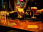 Barkeeper serviert farbenfrohe Cocktails an dunkler Theke in Hamburger Bar bei stimmungsvollem Licht.