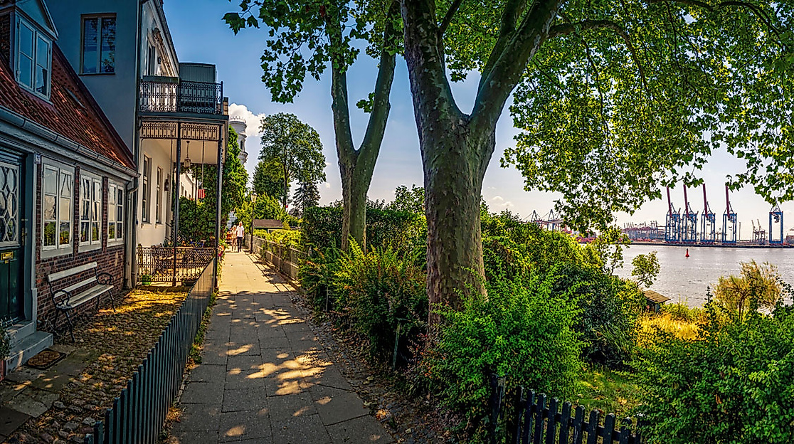 Elbewanderweg in Övelgönne mit Blick auf die Elbe, gesäumt von Häusern, Bäumen und Blick auf den Hafen
