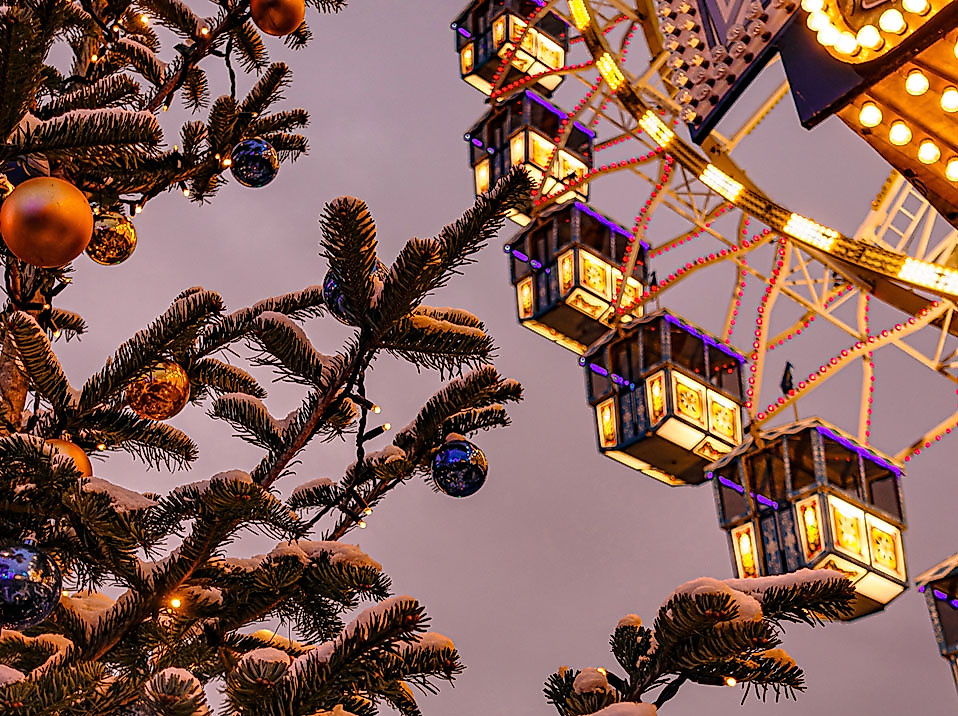 Beleuchtetes Riesenrad hinter verschneitem, geschmücktem Tannenbaum auf dem Winterdom