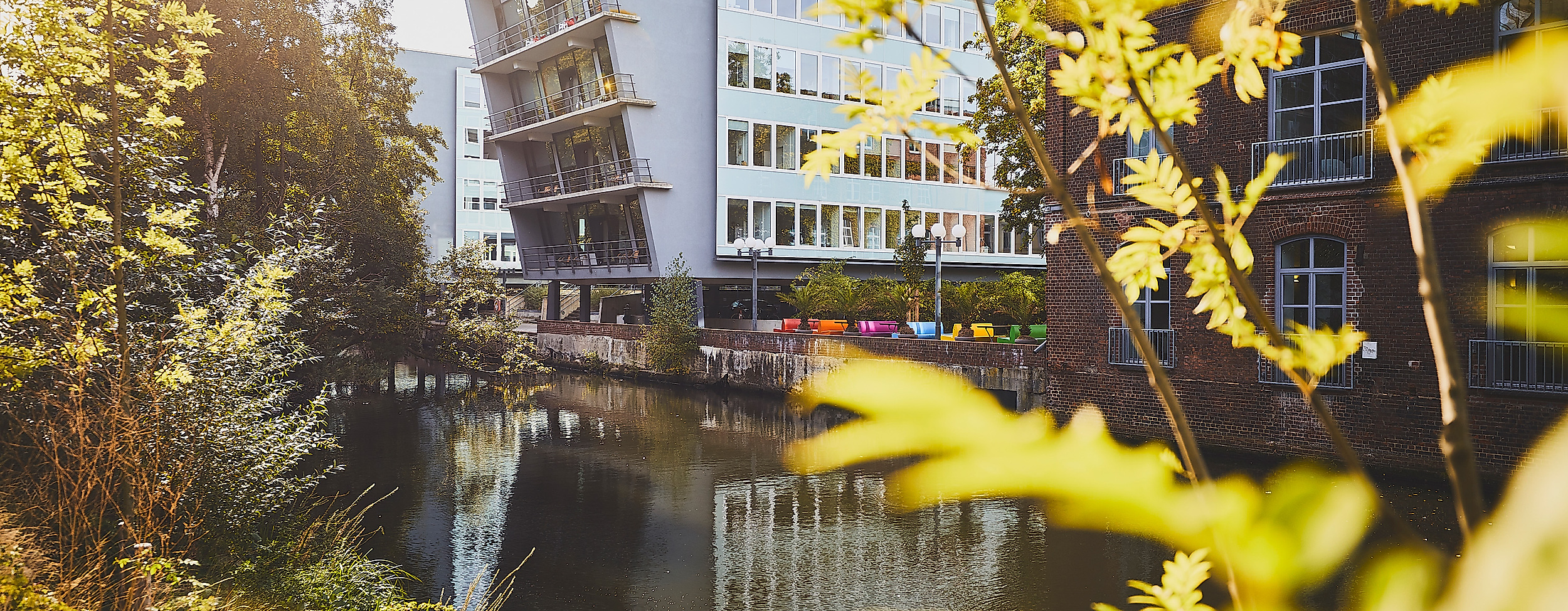 Harburger Theater am Kaufhauskanal in Hamburg, im Sonnenlicht durch Blätter mit Spiegelung im Wasser