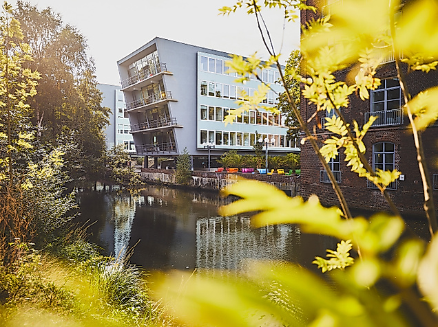 Harburger Theater am Kaufhauskanal in Hamburg, im Sonnenlicht durch Blätter mit Spiegelung im Wasser