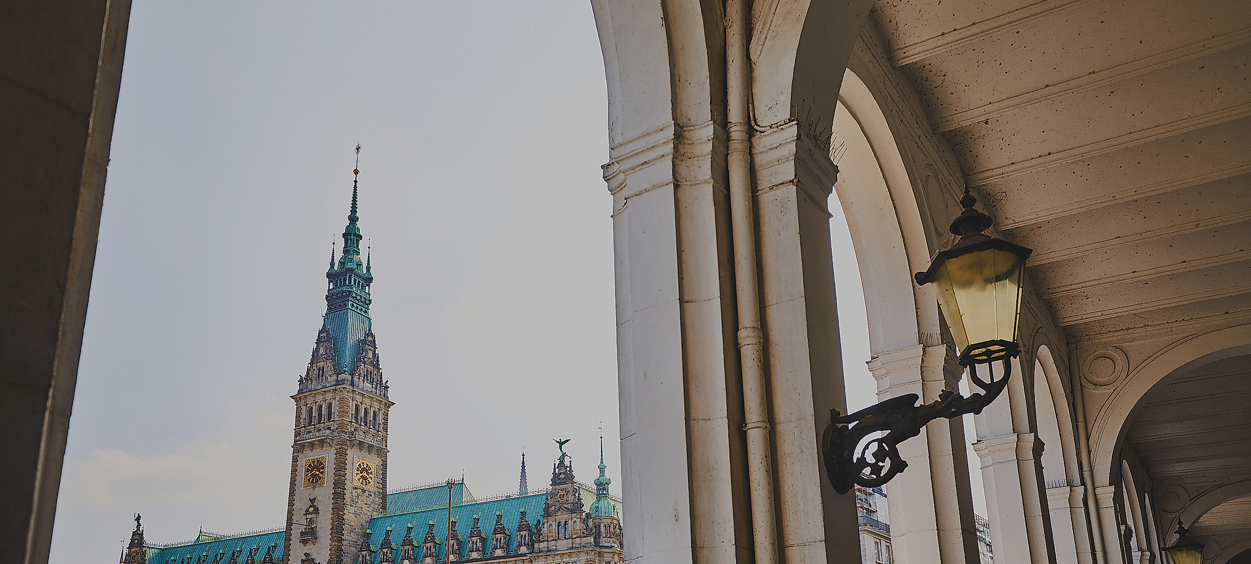 Blick durch die Alsterarkaden auf das Hamburger Rathaus mit grünem Kupferdach und Turm bei Tageslicht
