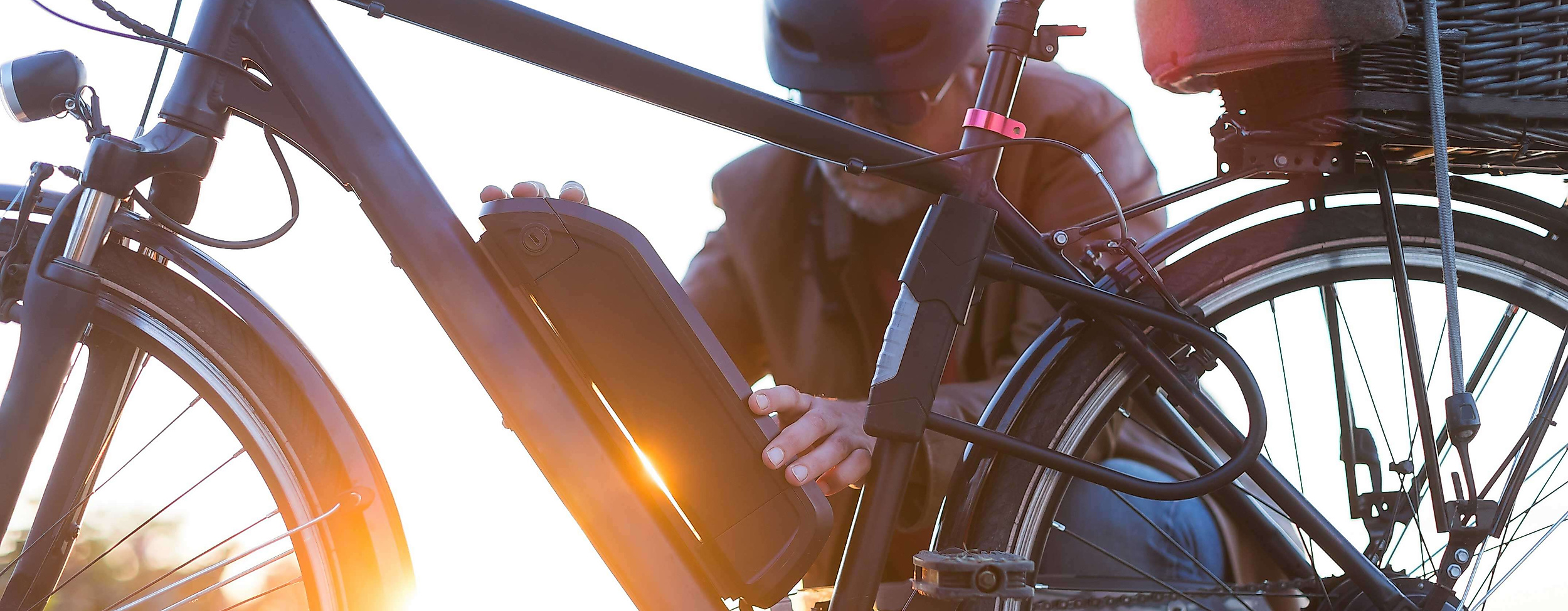 Person mit Helm prüft Akku an einem E-Bike bei Sonnenuntergang in urbaner Umgebung