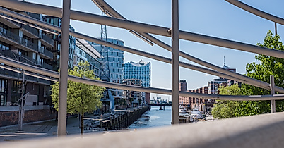 Blick durch Geländer auf Fleet in der HafenCity Hamburg mit moderner Architektur und blauem Himmel