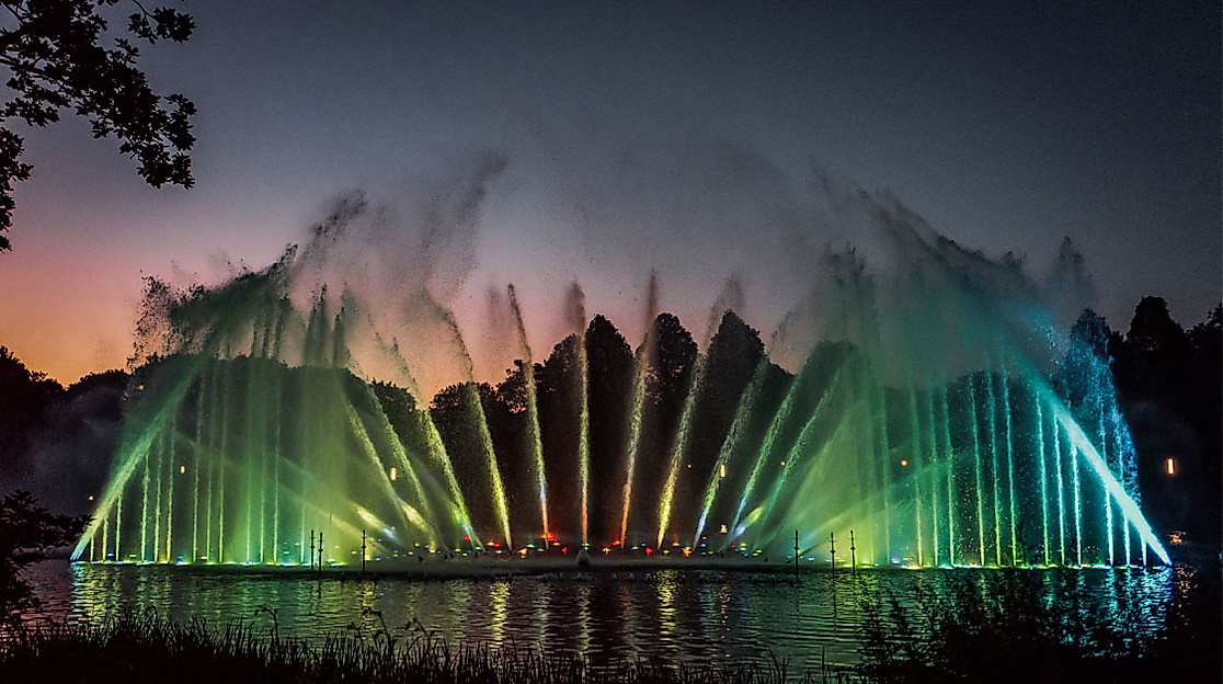 Farbige Wasserlichtshow bei Sonnenuntergang im Park Planten un Blomen spiegelt sich im See