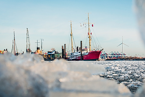 Historische Schiffe im verschneiten Hamburger Museumshafen mit Eisschollen im Vordergrund an einem Wintertag