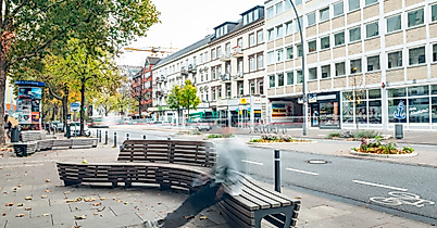 Fußgängerzone in Hamburg-Eimsbüttel mit modernen Holzbänken, Geschäften und herbstlich gefärbten Bäumen