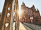 Sonnenlicht fällt durch eine Stahlbrücke auf ein historisches Speichergebäude am Sandtorkai in Hamburg
