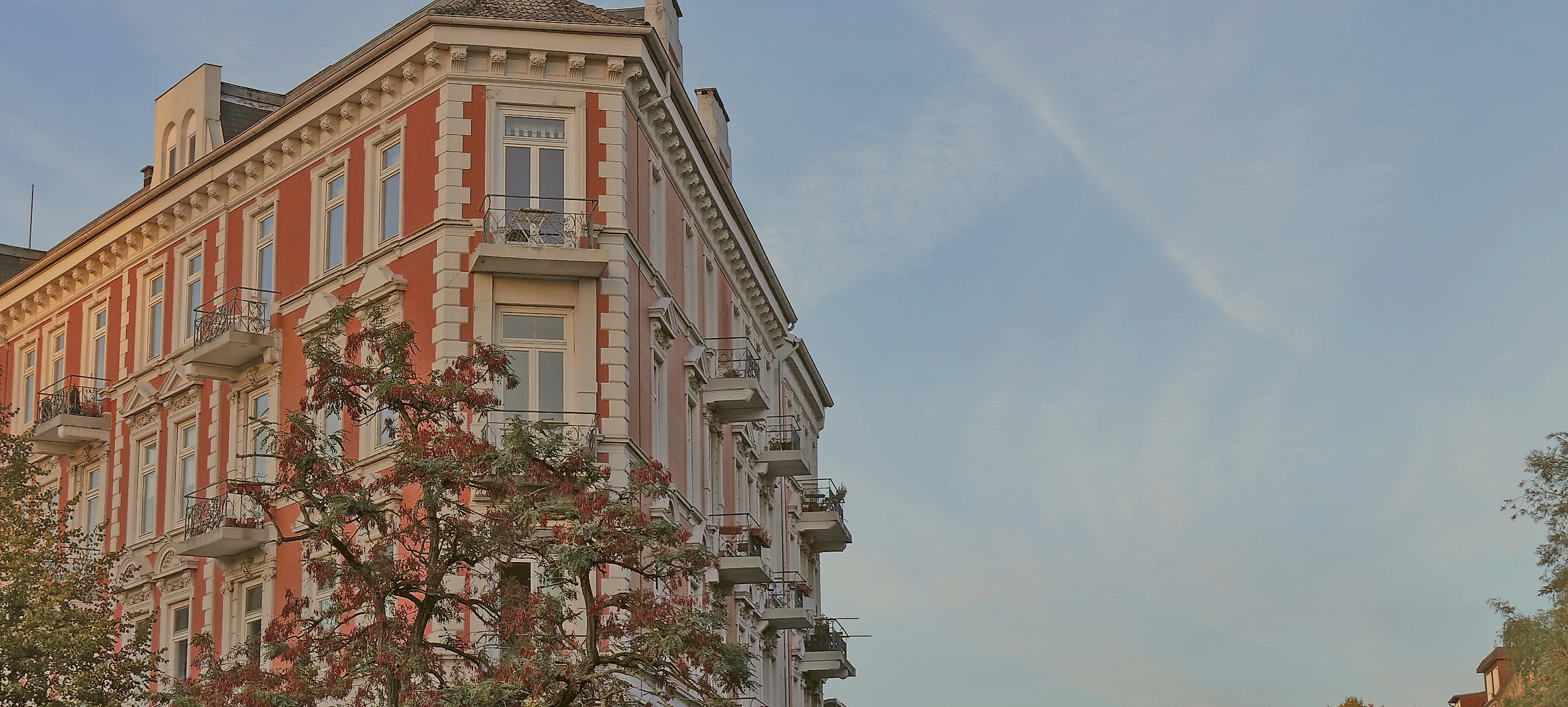 Historisches Gründerzeithaus in Hamburg im Abendlicht, flankiert von blühenden Bäumen und blauem Himmel