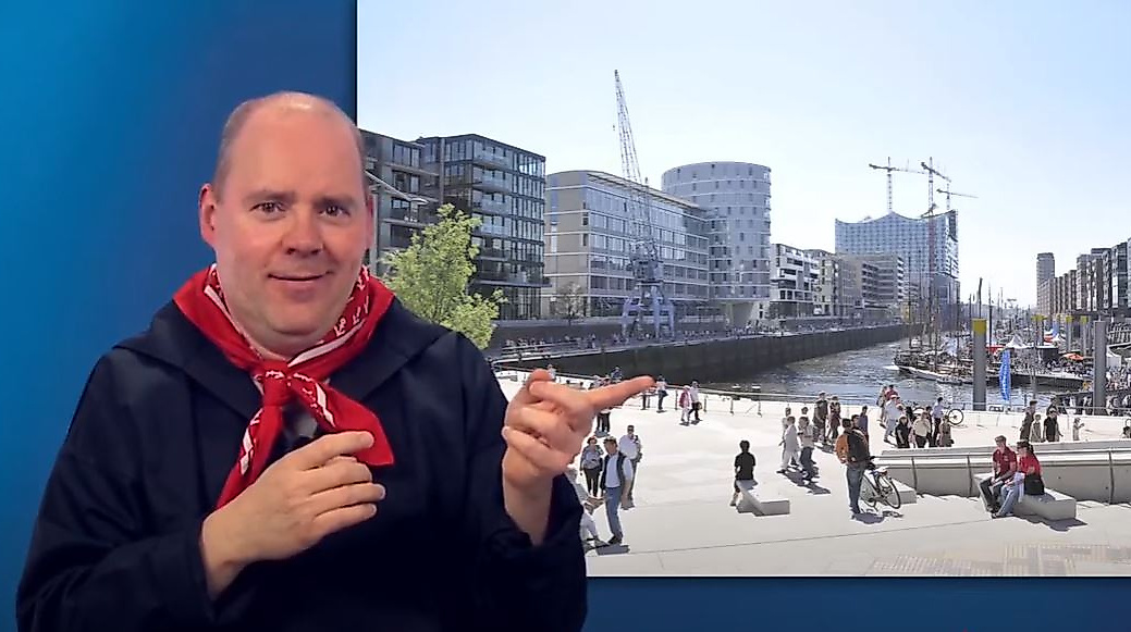 Mann gebärdet vor sonniger Promenade in der Hamburger HafenCity – barrierefreie Infos zum modernen Stadtteil.