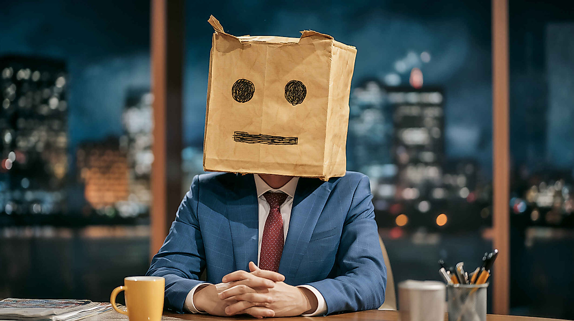 Talkshow-Moderator mit Papiertüte über dem Kopf auf die ein Gesicht gezeichnet wurde