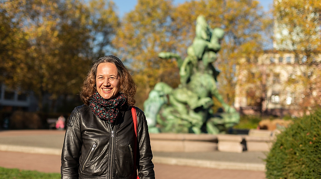 Frau im herbstlichen Park in Hamburg Altona-Ottensen vor bronzener Brunnenplastik