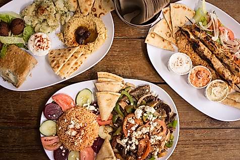 Griechische Spezialitäten wie Gyros, Souvlaki, Tzatziki und Fladenbrot auf drei Tellern serviert.
