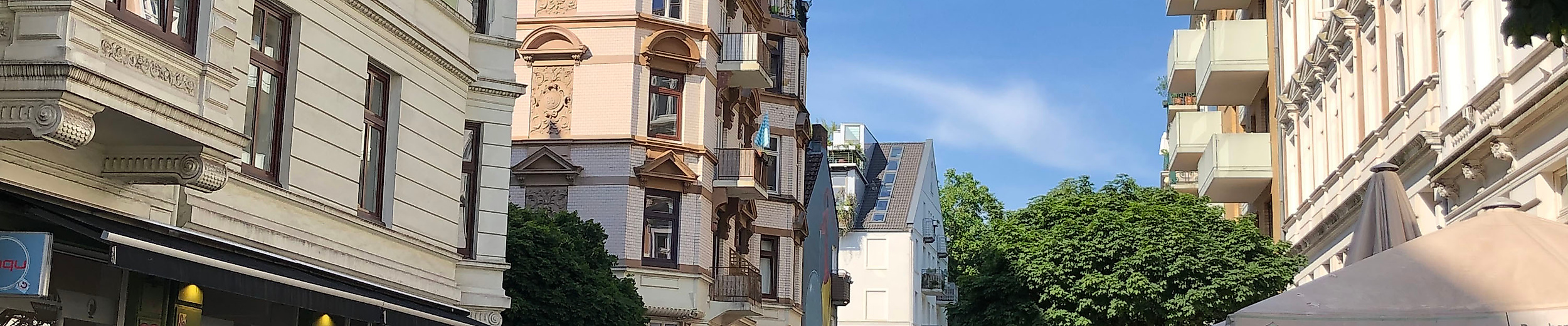 Belebte Schanzenstraße in Hamburg mit Altbauten, Straßencafés und kleinen Boutiquen bei Sonnenschein