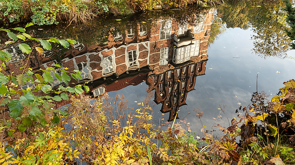 Spiegelung des Bergedorfer Schlosses im Wassergraben, umrahmt von herbstlicher Vegetation in Hamburg-Bergedorf.