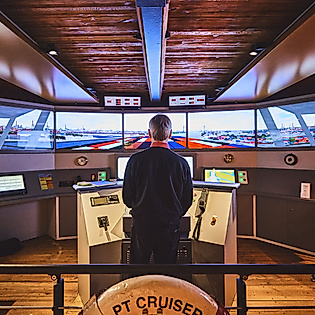 Person steuert einen Schiffsführungssimulator im Internationalen Maritimen Museum vor mehreren Monitoren
