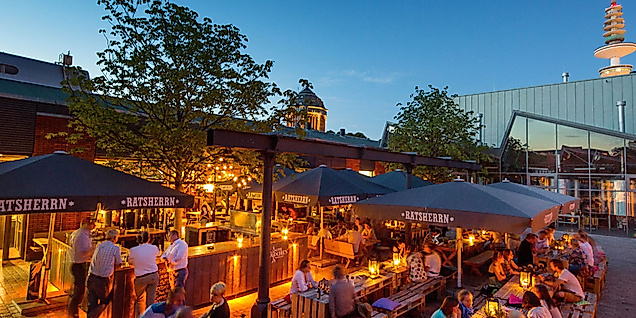 Belebter Außenbereich mit Bars und Gästen am Abend, im Hintergrund der Hamburger Fernsehturm