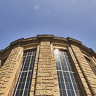 Historische Fassade des Alten Elbtunnels mit hohen Fenstern und Sonnenreflexen vor blauem Himmel