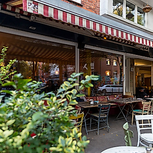 Außengastronomie eines Cafés in Hamburg mit rot-weißer Markise, Holztischen und umgebendem Grün