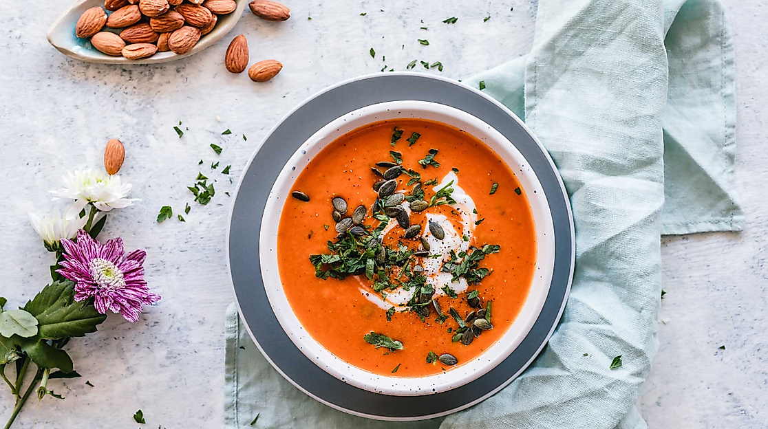 Cremige Tomatensuppe mit Sahne und Kräutern in Schale, daneben Mandeln und Blumen dekorativ angerichtet