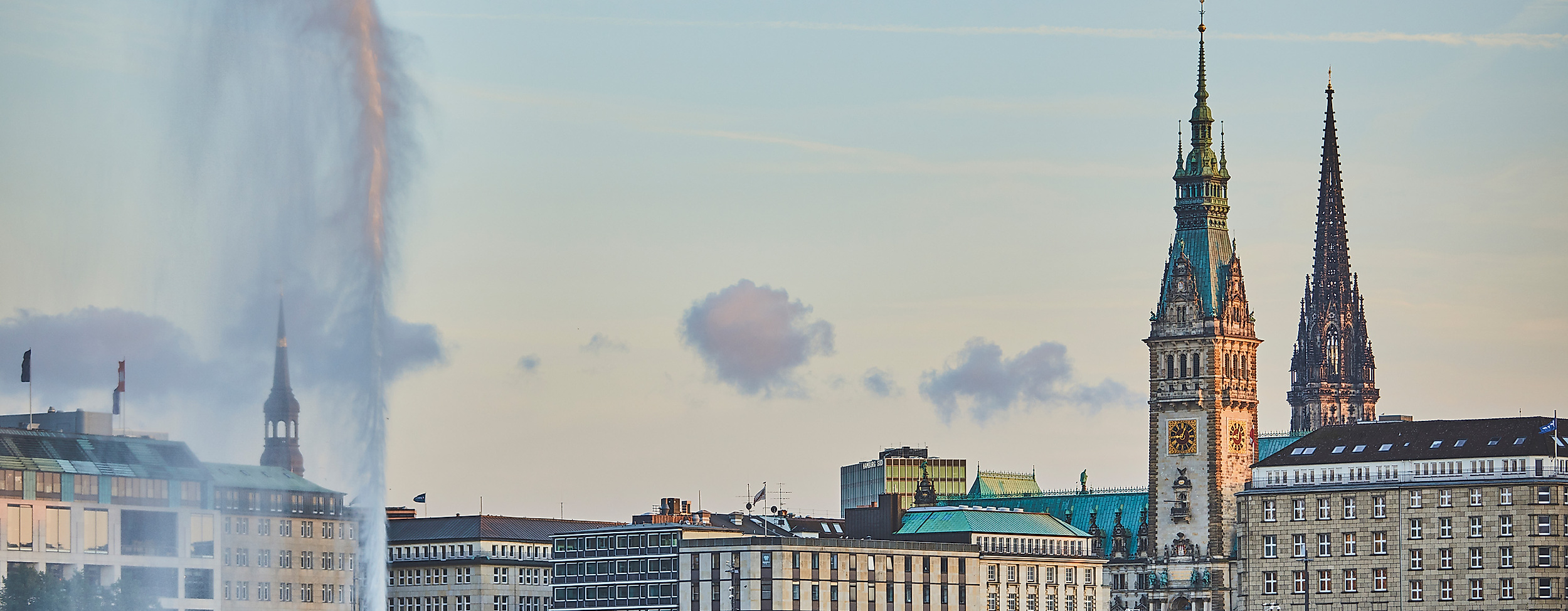 Blick über die Binnenalster auf das Hamburger Rathaus und die Alsterfontäne bei Abendlicht