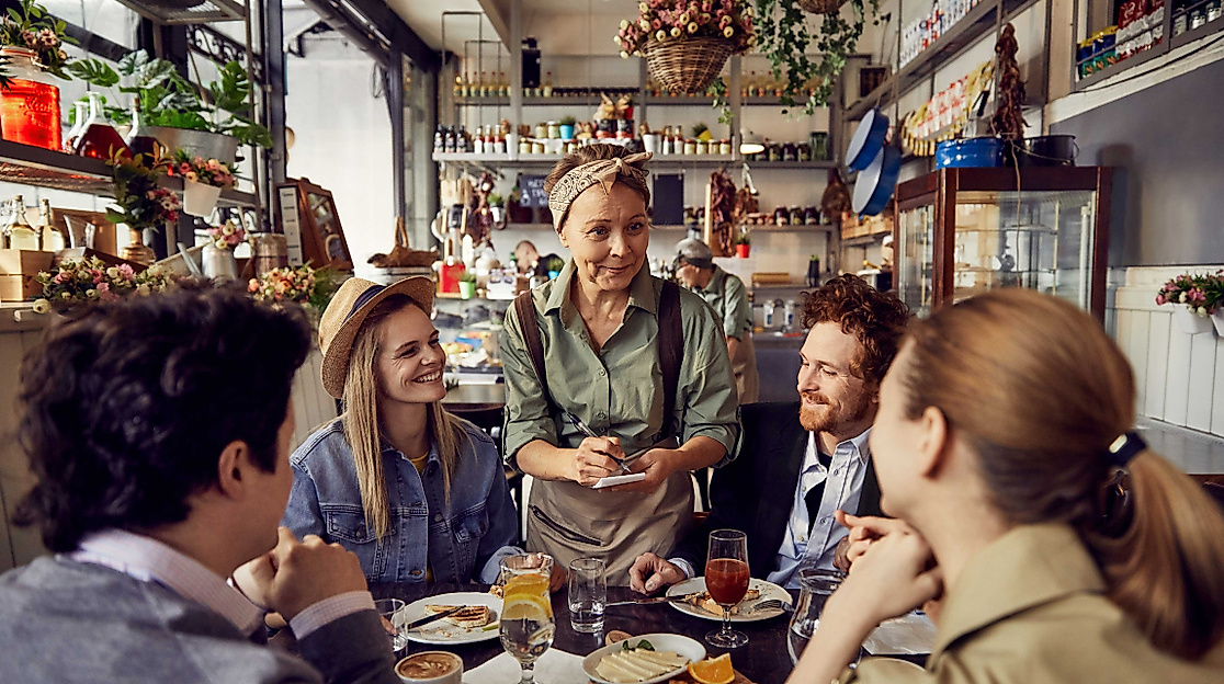 Bedienung, die von 4 Menschen in einem Restaurant die Bestellung aufnimmt. 