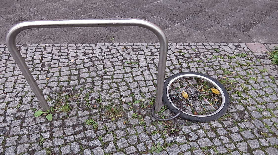 Zurückgelassenes Fahrradlaufrad mit Schloss an Fahrradständer auf Kopfsteinpflaster