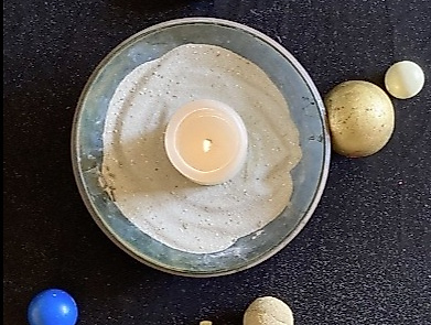 brennende Kerze in einer Sandschale mit Kreuz und Perlen von oben