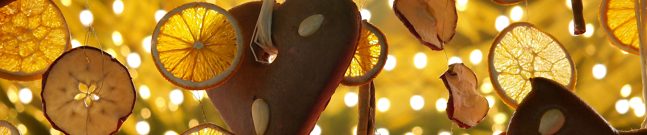 Weihnachtsdeko aus Orangenscheiben und Holzanhängern vor Lichterglanz am Tannenbaum