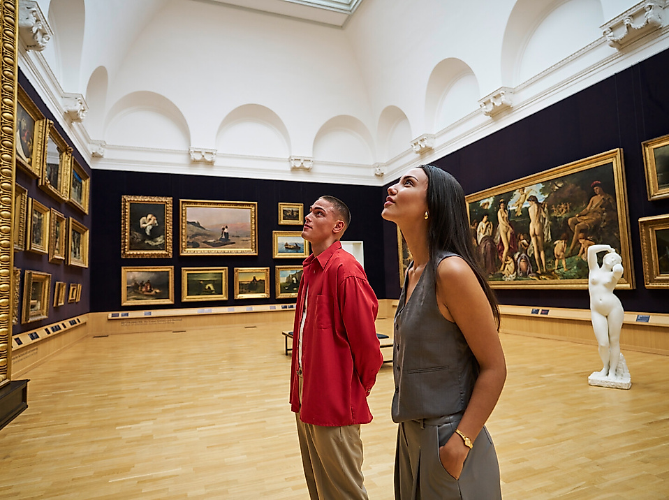 Zwei junge Erwachsene betrachten Bilder in einem historischen Saal der Kunsthalle Hamburg.