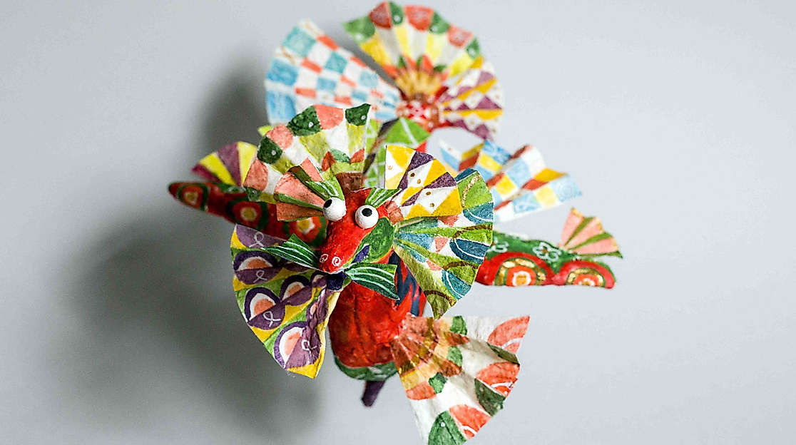 Spielerischen Charme und handwerkliches Können verbindet die russische Künstlerin Kira Kotliar bei farbenfrohen Kleinplastiken aus bemaltem Pappmaché wie dem farbenfrohen Drachen.