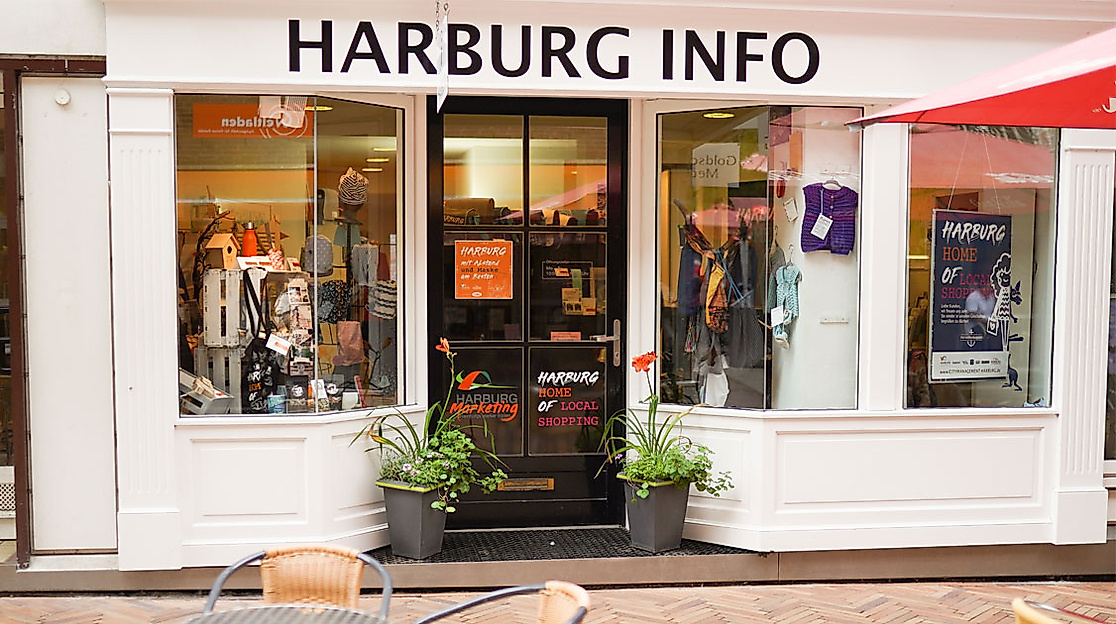 Eingang der Tourist-Information „Harburg Info“ in Hamburg-Harburg mit Schaufenstern, Plakaten und Blumen vor der Tür
