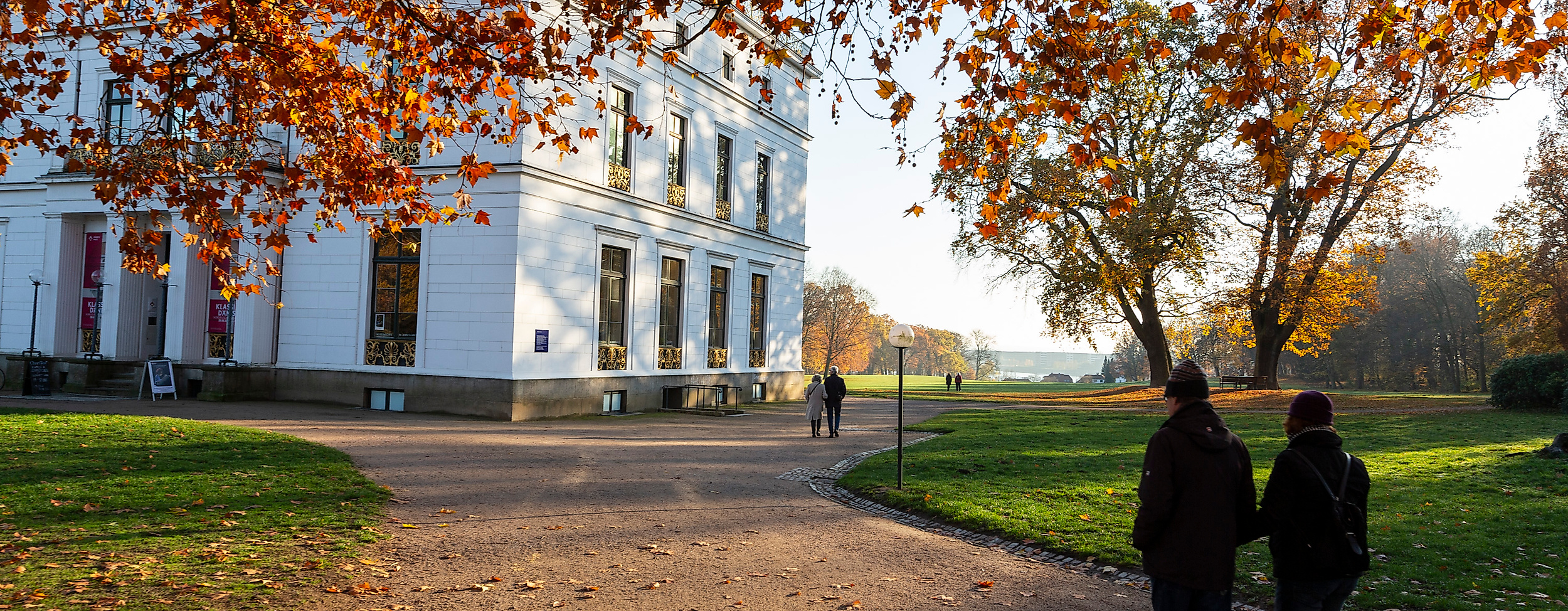 Spaziergänger:innen im herbstlichen Hirschpark Hamburg-Blankenese vor dem weißen Jenisch Hauss