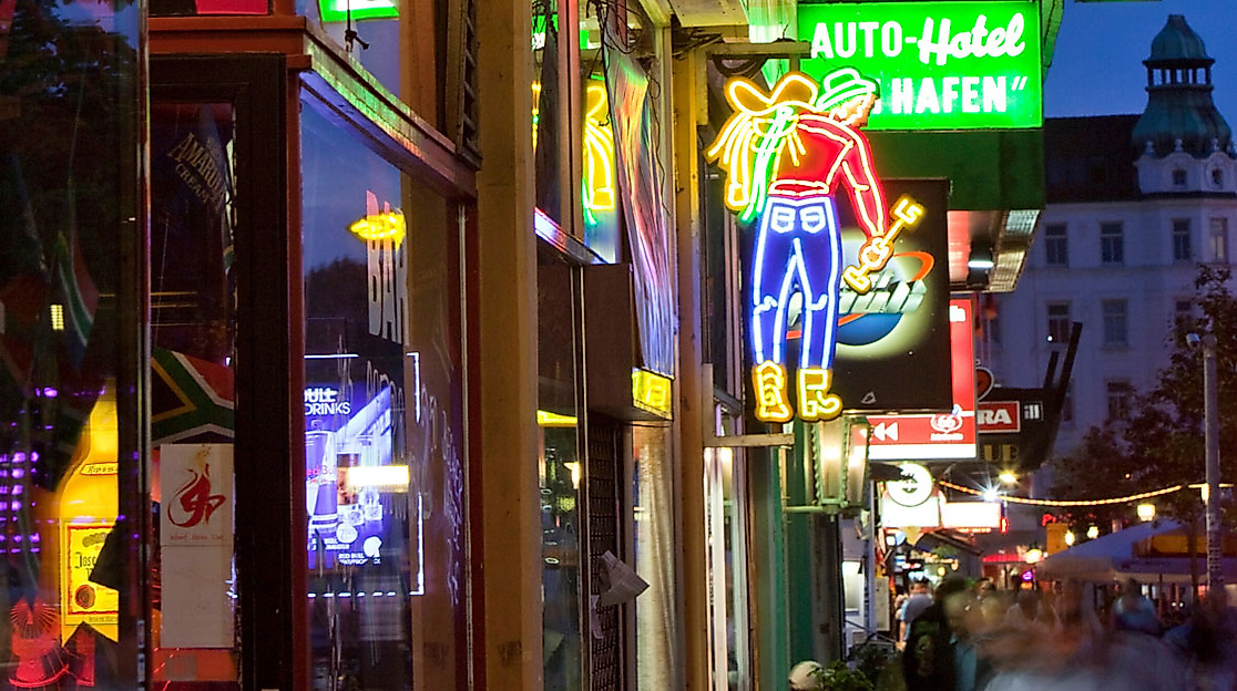 Leuchtende Neonreklamen und Schilder auf der Reeperbahn in Hamburg bei Abenddämmerung mit belebter Straße