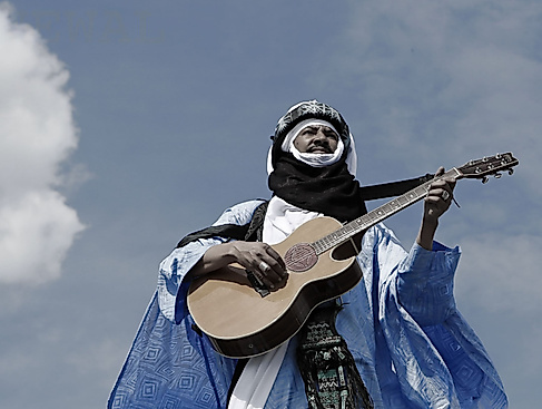 Alhousseini Anivolla steht mit einer Gitarre auf einem Hausdach. Im Hintergrund ist der Himmel zu sehen.