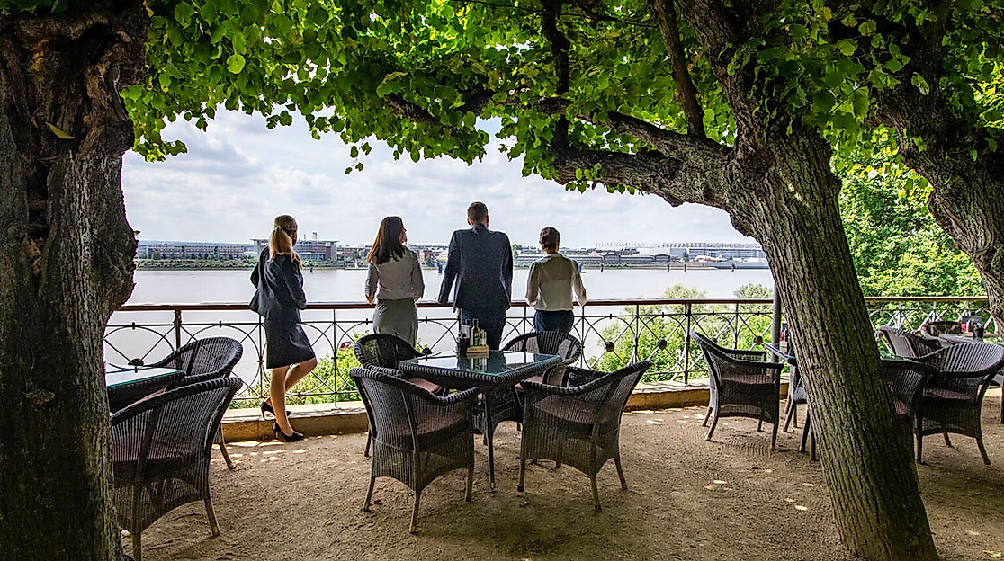 Lindenterrasse des Hotel Louis C. Jacob mit Blick auf die Elbe, schattigen Sitzplätzen und Gästen am Geländer