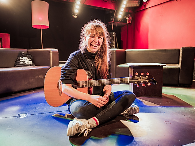 Musikerin mit Gitarre sitzt auf dem Boden des Clubs Molotow, bunte Lichtspots im Raum