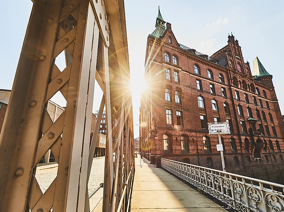 Sonnenlicht fällt durch eine Stahlbrücke auf ein historisches Speichergebäude am Sandtorkai in Hamburg