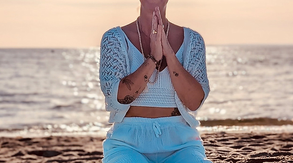 Frau und Yogalehrerin am Strand beim Yoga in Haffkrug und Scharbeutz. Hände vor dem Herzen in Namasté Haltung verbunden. Ostsee glitzert im Hintergrund
